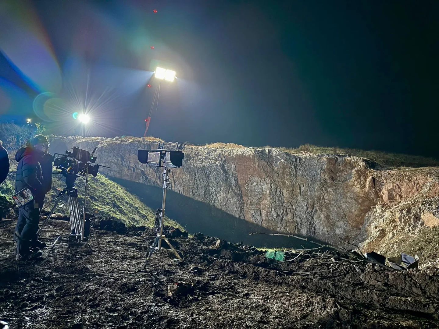 Night shoot at a quarry edge, with crew, camera and monitors lit by floodlights on a tall mast.